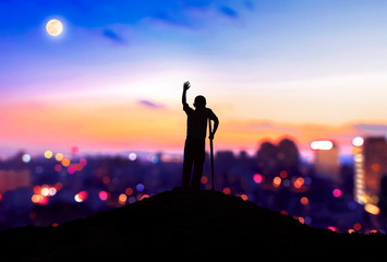 International Day of Persons with Disabilities concept： Silhouette a disabled man standing at mountain city background