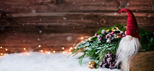 Weihnachtswichtel sitzt auf einem Holzbrett in winterlichter Dekoration und wartet auf Weihnachten - Banner, Header, Headline - Format