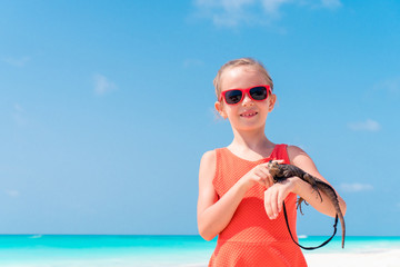 Adorable little girl happily holds a wild tropical lizard on white tropical beach