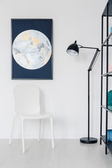Vertical view of white chair in white interior with moon graphic on the wall and metal lamp, real photo