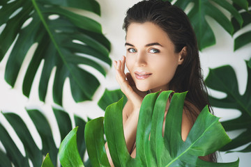 Portrait of young and beautiful woman with perfect smooth skin in tropical leaves