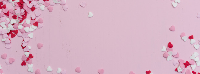 Panoramic website banner image with many tiny heart-shaped sugar sprinkles in red, white and pink with space for copy text or romantic love message for Valentine's Day on February 14th, flat lay