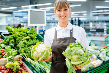 Shop assistant woman in supermarket showing the fresh produce with pride looking into camera