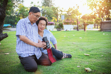 Cheerful asian senior couple enjoying with photography in the park with a retro camera