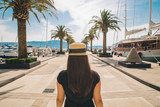 woman walk by sunny pier with palms. mountains and yachts on background