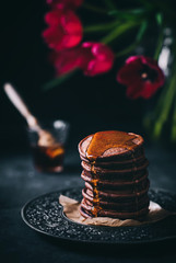 Schokoladige Pancakes mit Ahornsirup auf dunklem Untergrund mit roten Tulpen im Hintergrund