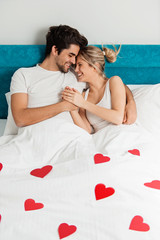 Young loving couple lying on the bed with hearts, enjoying