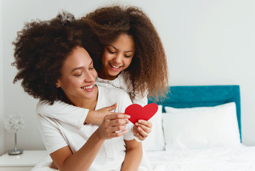 Mother and daughter enjoying on the bed, holding red hearts 