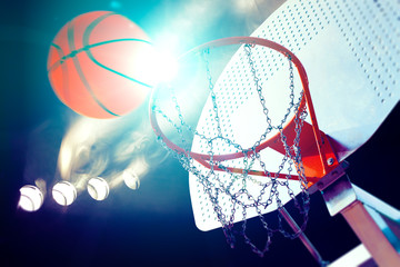 Deportes y entretenimiento. Baloncesto y deportes de equipo.Canasta  y pelota iluminados por los focos. Partido y evento deportivo. Público y multitud aplaudiendo el partido de baloncesto.