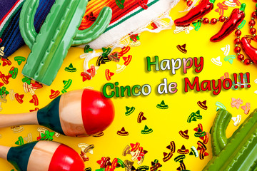 Mexican fiesta and latino party concept theme with jalapeno pepper necklace, maracas, cactus and traditional rug covered in sombrero shaped confetti on yellow background with Happy Cinco de Mayo text