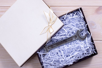 Gift box on wooden light background. Wrench. Unexpected gift