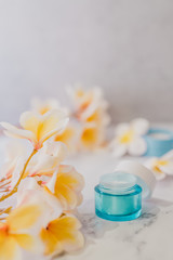 group of skincare products including moisturiser and scrub pots on marble table with exotic frangipani flowers