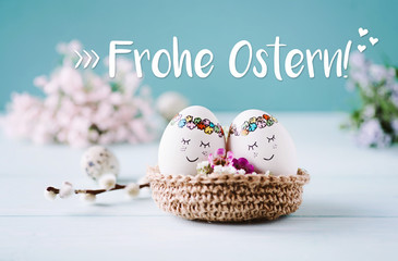 Zwei Ostereier mit süßen Gesichtern kuscheln in einem Osternest / blauer Hintergrund - Frohe Ostern!