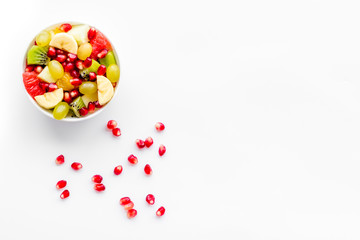 Fruit diet concept. Fruit salad with apple, kiwi and pomegranate in bowl on white background top view copy space