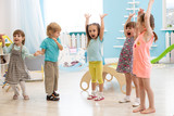 Group of expressive preschool children with raising hands while having fun in entertainment center