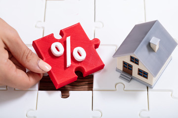 Person Holding Percentage Puzzle Pieces Near The House Model