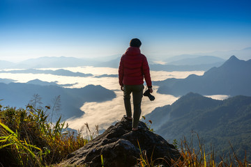 Photographer hand holding camera and standing on top of the rock in nature. Travel concept.