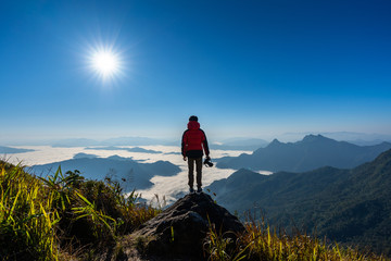 Photographer hand holding camera and standing on top of the rock in nature. Travel concept.
