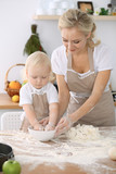 Little girl and her blonde mom in beige aprons playing and laughing while kneading the dough in kitchen. Homemade pastry for bread, pizza or bake cookies. Family fun and cooking concept