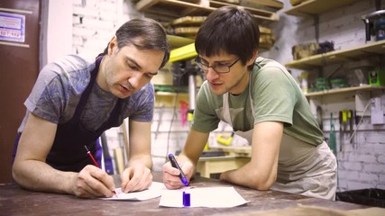 Two carpenters discuss drawing (round wood) in the workshop
