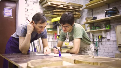 Two carpenters discuss drawing (round wood) in the workshop