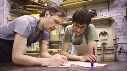 Two carpenters discuss drawing (round wood) in the workshop