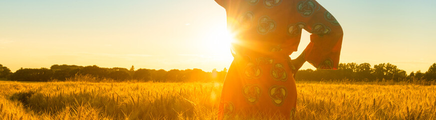 African woman in traditional clothes standing in a field of crops at sunset or sunrise