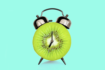 Kiwi slice on alarm clock, blue pastel background. fruit and vitamins diet at breakfast nutrition concept