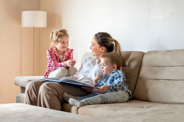 Happy mother enjoying day with children while reading book together at home