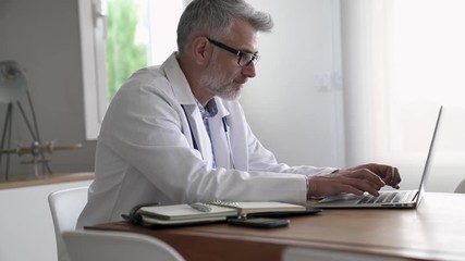 Mature doctor in office working on laptop computer