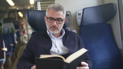 Mature man reading book while traveling on a train