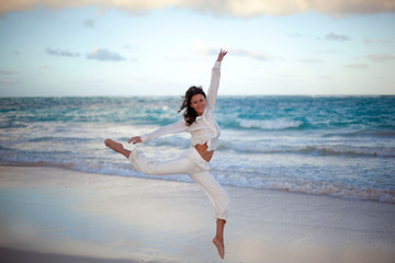Young beautiful woman is dancing wearing white clothes suit on sunset in tropical beach