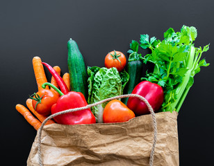 fresh organic vegetables in brown paper bag against dark table background