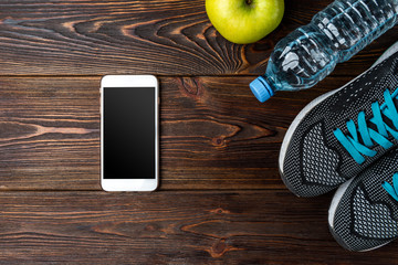 Fitness sneakers, bottle of water, apple and mobile phone on dark wooden background. 