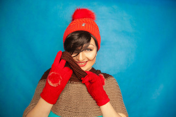 pretty brunette girl wearing fashion red knitted winter gat and warm beautiful gloves on blue studio solid background