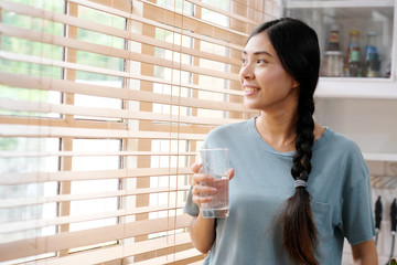 Youn beautiful asian woman drinking water while standing by window in kitchen background, peolpe and healthy lifestyles