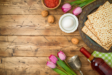 Jewish holiday Passover background with matzo, seder plate, wine and tulip flowers on wooden table.