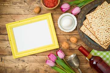 Jewish holiday Passover background with matzo, seder plate, wine, tulip flowers and photo frame on wooden table.