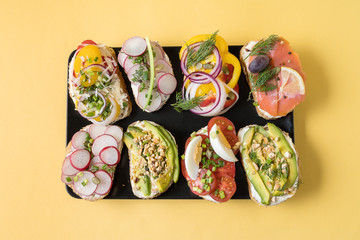 Sandwiches prepared with cream cheese and vegetables and salmon, on black plate, over yellow background. Healthy food for lunch or breakfast. Copy space, flat lay.