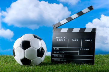 Fußball und Hollywood Filmklappe auf grünem Rasen vor weißblauem Wolkenhimmel