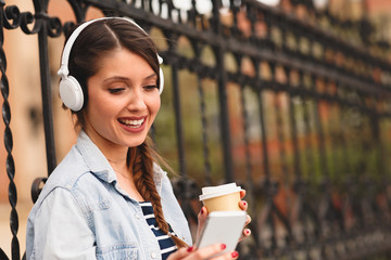 Young woman listens to music via headphones and smartphone in the city