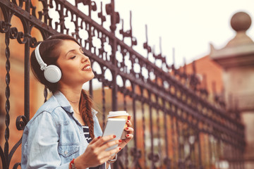 Young woman listens to music via headphones and smartphone in the city