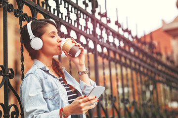 Young woman listens to music via headphones and smartphone in the city