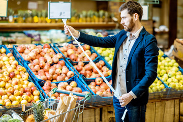 Portrait of an elegant man holding very long shopping list while buying food in the supermarket