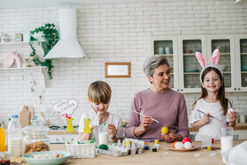 Waist up portrait of happy children and their grandmother coloring Easter eggs
