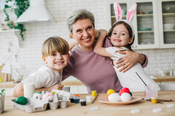 Half length of gray-haired woman hugging her grandchildren in kitchen