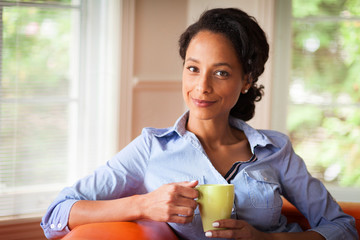 African Woman sitting on her sofa in her living room holding a cup . She relaxing .