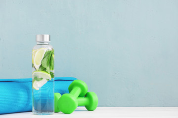 Water with lemon and mint in the glass bottle and green dumbbells