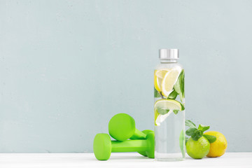 Water with lemon and mint in the glass bottle and green dumbbells