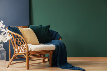 Blanket and pillows on rattan sofa in green and blue living room interior with flowers. Real photo